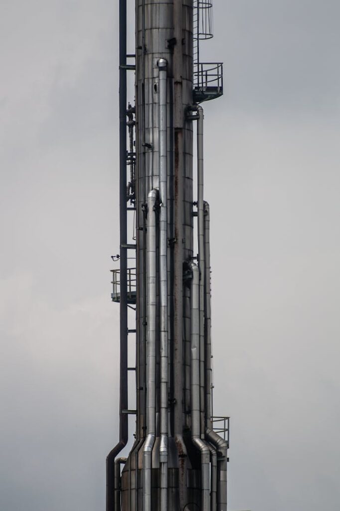 Close-up of a tall industrial chimney structure with metallic pipes under a cloudy sky.
